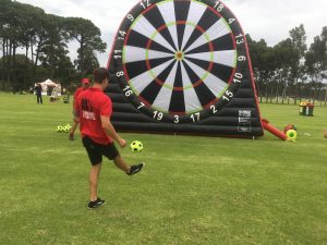A young boy named Bronny kicks a soccer ball at a giant inflatable dartboard.