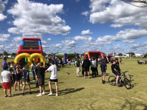 Kids race across a Ninja Warrior inflatable obstacle course at an outdoor event.