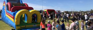 A brightly colored inflatable Ninja Warrior obstacle course with children and a crowd gathered around.