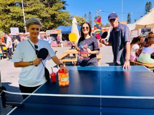 A crowd of people playing and watching table tennis at a lively event in Fremantle Esplanade.