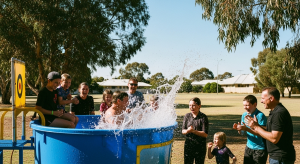 An ultra-realistic, 4K, and grainy photograph of people and kids playing in a blue dunk tank at an event in Jandakot, Western Australia.